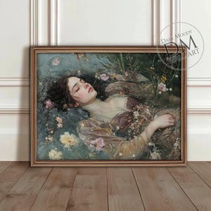 Puede incluir: Una obra de arte enmarcada representa a una mujer flotando en el agua, rodeada de flores. La pintura presenta una paleta de colores apagados con tonos de marrón, rosa y azul. La obra está etiquetada como "Dark Moody Wall Art".