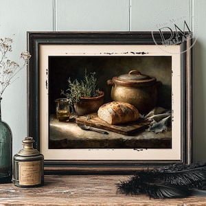 Op de afbeelding: Ingelijste kunstafdruk met een stilleven van een rustieke keuken. Een brood ligt op een houten plank naast een pot, een klein glaasje olie en een kruidenplant in pot. Het kunstwerk heeft een donkere, sfeervolle esthetiek.