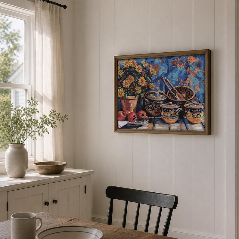 May include: A framed still life painting depicts a table setting with ceramic pots, apples, and a flower arrangement. The artwork features a wooden frame and is displayed on a white wall in a dining room setting.