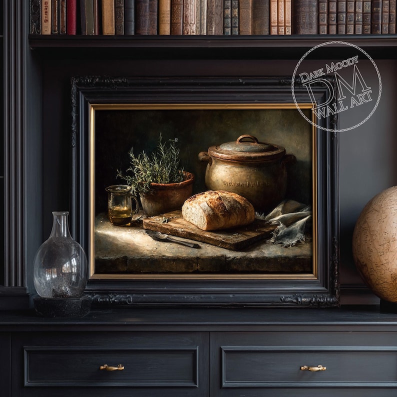 Op de afbeelding: Een ingelijst stilleven schilderij met een brood op een houten plank, een kleipot en een kleine glazen pot. Het kunstwerk heeft een donkere, melancholische esthetiek met warme tinten en een vintage uitstraling. Het schilderij is ingelijst in een zwart frame.