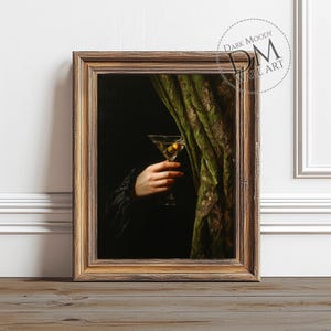 Könnte beinhalten: Gerahmter Kunstdruck mit einer Hand, die ein Martiniglas mit einer Olive hält. Das Kunstwerk hat eine dunkle, stimmungsvolle Ästhetik mit einem grünen Vorhang und einem goldfarbenen Rahmen. Der Text "DARK MOODY WALL ART" ist sichtbar.