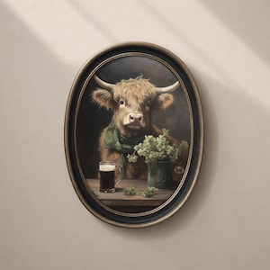 May include: Oval framed artwork featuring a Highland cow wearing a green scarf, with a pint of dark beer and a vase of greenery on a wooden table. The cow has long, shaggy brown fur and large horns. The frame is black with a gold inner edge.