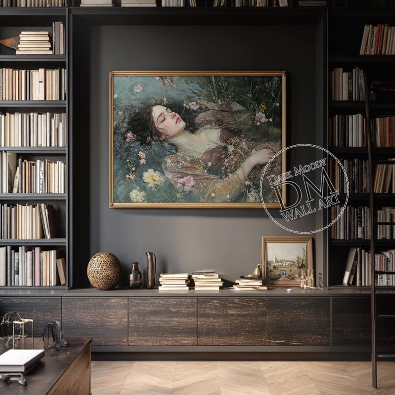 May include: A framed wall art print featuring a woman in a flowing gown, floating in water amidst flowers. The artwork has a gold frame and is displayed on a dark gray wall. The print is surrounded by bookshelves and decorative items.