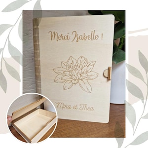 May include: A wooden box with a hinged lid. The lid is engraved with the text "Merci Isabelle!" and a stylized flower design. The bottom of the box is engraved with the text "Mika et Thea".