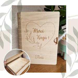 May include: A wooden box with a hinged lid. The box is engraved with the words "Merci Kenza!" inside a heart shape with floral accents. The name "Thea" is engraved below the heart.