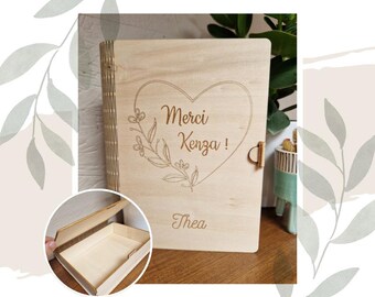 Puede incluir: Una caja de madera con tapa con bisagras. La caja está grabada con las palabras "Merci Kenza!" dentro de un corazón con acentos florales. El nombre "Thea" está grabado debajo del corazón.