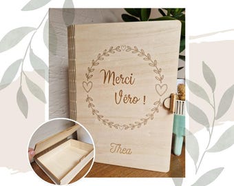 Puede incluir: Una caja de madera con tapa abatible. La caja está grabada con el texto "Merci Vero!" y "Thea" en una fuente decorativa. La caja está decorada con una corona de hojas y corazones.