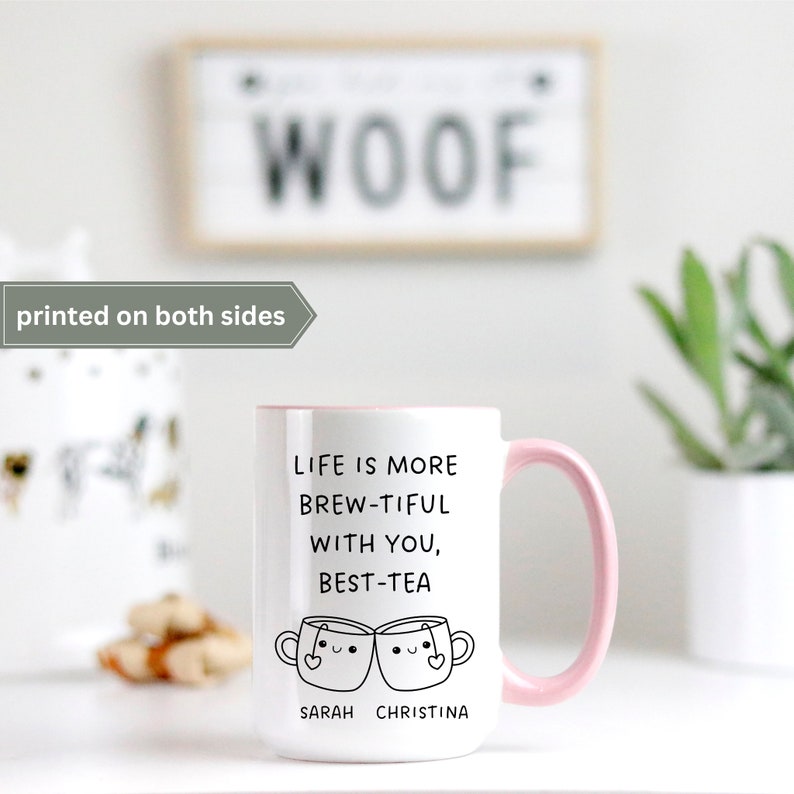 May include: White ceramic mug with a pink rim and handle. The mug has a black graphic that says "Life is more brew-tiful with you, best-tea" with two cartoon teacups with faces. The text "Sarah Christina" is below the teacups.