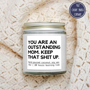 May include: A clear glass candle jar with a silver lid, featuring a white label with black text that reads "YOU ARE AN OUTSTANDING MOM. KEEP THAT SHIT UP." The label also states "Hand-poured coconut soy wax 113g | 20 hours burning time."