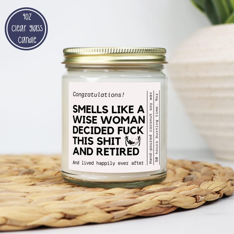 May include: A clear glass candle jar with a gold lid. The label reads "Smells Like a Wise Woman Decided Fuck This Shit and Retired." The candle is hand-poured coconut soy wax and has a 50-hour burn time. A blue circle indicates the candle is 9oz.