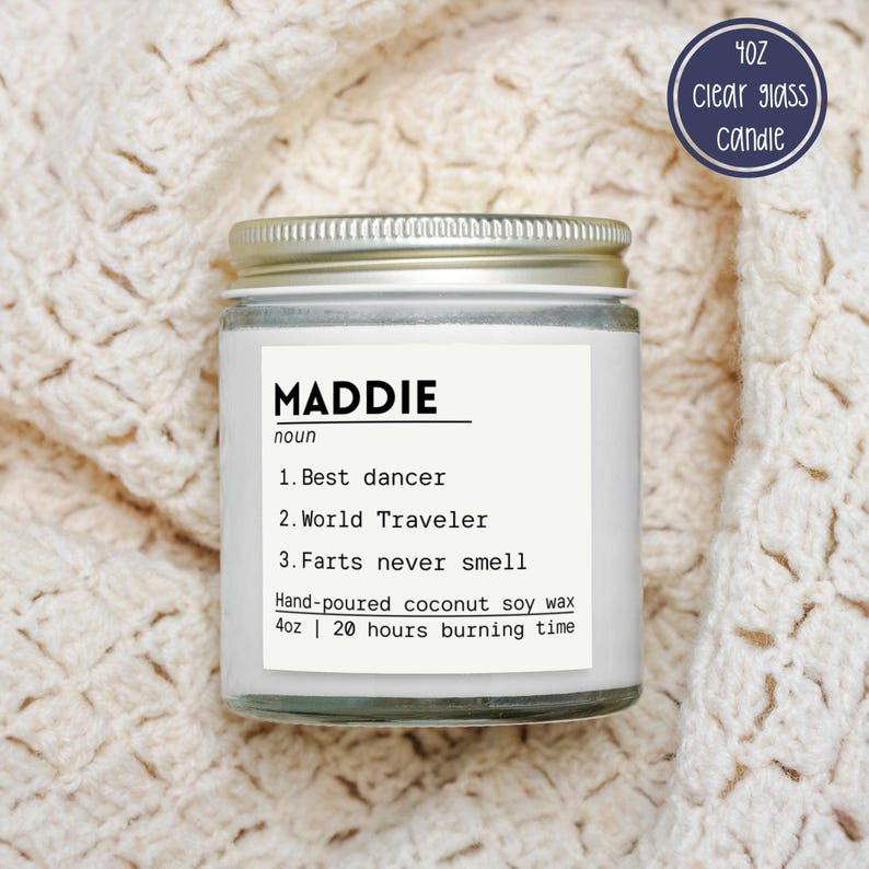May include: A 4oz clear glass candle with a silver lid and a white label. The label features the text MADDIE noun, 1. Best dancer, 2. World Traveler, 3. Farts never smell, Hand-poured coconut soy wax, 4oz | 20 hours burning time.