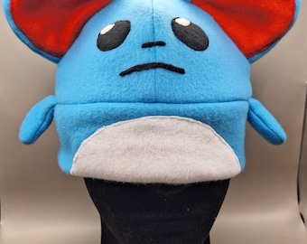 May include: Blue and white plush hat shaped like a cartoon mouse with large red ears. The hat has a white belly and black eyes and mouth.