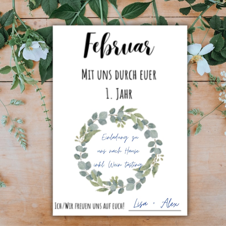 May include: A white card with the text "Februar" in black cursive lettering. The text "MIT UNS DURCH EUER 1. JAHR" is below the title. A wreath of green eucalyptus leaves surrounds the text "Einladung zu uns nach Hause inkl Wein tasting". The text "ICH/WIR FREUEN UNS AUF EUCH!" is below the wreath. The names "Lisa Alex" are written in blue cursive lettering below the text.