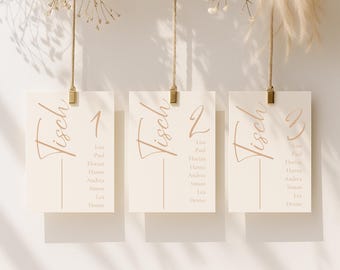May include: Three rectangular off-white cards hanging from jute twine with gold clips. Each card features the word Tisch, a large number, and a list of names including Lisa, Paul, Florian, Hanna, Andrea, Simon, Lea, and Denise in brown text.