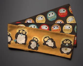 May include: Two fabric panels with a repeating pattern. The top panel is brown with a white star pattern and features a repeating pattern of red, yellow, and blue daruma dolls. The bottom panel is yellow with a repeating pattern of brown bears wearing hats and holding objects.