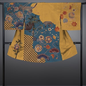 May include: A traditional Japanese kimono in mustard yellow and teal. The garment is decorated with floral and geometric patterns, and illustrations of cats. The kimono is displayed on a black metal rack. The design is intricate.