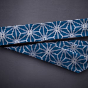 Puede incluir: Dos corbatas azules con un patrón geométrico blanco. Las corbatas están dobladas y colocadas sobre una superficie gris.