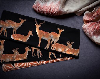 May include: Two black fabric panels with a repeating pattern of brown deer printed on them. The fabric is folded in thirds, and the panels are lying on a grey surface.