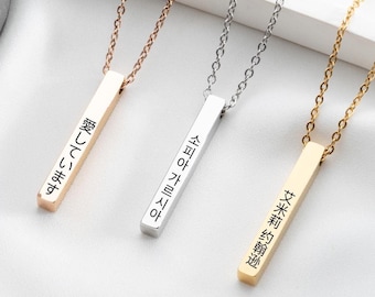 May include: Three gold bar necklaces with different languages inscribed on them. The necklaces are on a white surface. The languages are Japanese, Korean, and Chinese.