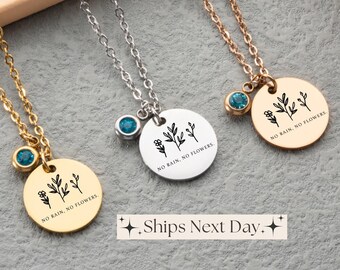 May include: Three gold, silver, and rose gold necklaces with a round pendant that says "NO RAIN, NO FLOWERS." Each pendant has a small blue gemstone.