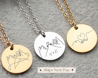 May include: Three gold necklaces with round pendants featuring a line drawing of two hands intertwined with a heart. One pendant has the initials "N & K" inscribed on it.