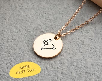 May include: A gold-colored necklace with a round pendant featuring a black treble clef heart design. The chain is also gold-colored. The necklace is displayed on a gray surface.