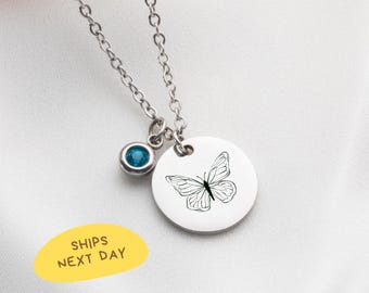 May include: A silver-colored necklace with a round pendant featuring a black butterfly design. A small, round, blue gemstone hangs near the pendant. The text "SHIPS NEXT DAY" is on a yellow oval.