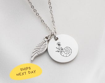 May include: A silver-colored necklace with a chain, a leaf-shaped charm, and a round pendant. The pendant features a black line drawing of a flower and a spiral. The text "SHIPS NEXT DAY" is on a yellow oval.