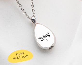 May include: Silver-toned teardrop pendant necklace with a delicate dragonfly design. The pendant hangs from a fine chain. The dragonfly is black and detailed. The necklace is displayed on a white surface.
