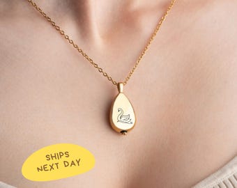 May include: Gold-colored pendant necklace with a teardrop-shaped charm. The charm features a swan design and hangs from a delicate chain. The text "SHIPS NEXT DAY" is in a yellow oval.