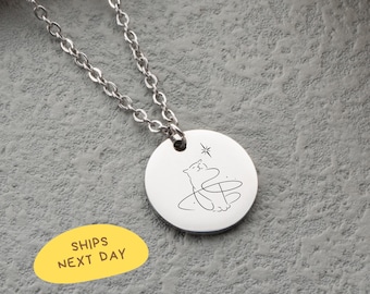 May include: A silver-colored necklace with a round pendant featuring a whimsical cat design and a star. The chain is a delicate link style. The pendant has a black line drawing of a cat. The text "SHIPS NEXT DAY" is on a yellow oval.