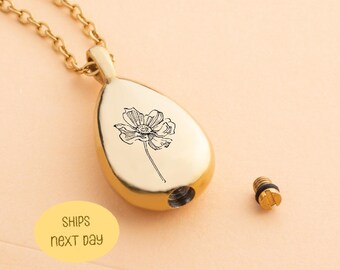 May include: A gold-colored teardrop-shaped pendant necklace with a black floral design. The pendant has a screw-on cap and is on a gold chain. The text "SHIPS next DAY" is in a yellow oval.