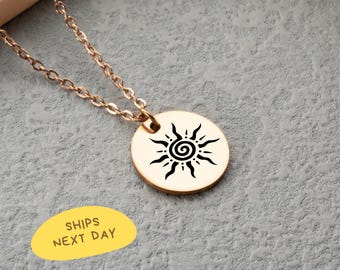 May include: A rose gold necklace with a circular pendant featuring a black sun design. The chain and pendant are visible against a gray background. The pendant has a spiral center with radiating lines. The text "SHIPS NEXT DAY" is in a yellow oval.