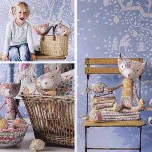 May include: A collection of handcrafted fabric cat dolls featuring various floral and patterned textiles in soft pastel colors. The dolls have pointed ears, long tails, and stitched facial features, displayed alongside woven baskets and a wooden chair.