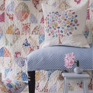 May include: A white quilted pillow featuring a colorful tree applique with patterned leaves, placed on a blue and white polka dot chair. The chair is set against a large, matching white quilt with a repeating circular floral patchwork design.