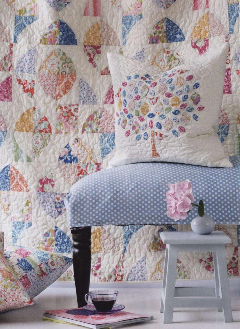 May include: A white quilted pillow featuring a colorful tree applique with patterned leaves, placed on a blue and white polka dot chair. The chair is set against a large, matching white quilt with a repeating circular floral patchwork design.