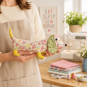May include: A stuffed dachshund toy made from floral patterned fabric with a cream base, featuring yellow polka-dot fabric on the tail and feet, and green floral fabric on the ears. The toy has a black nose and round black and white eyes.