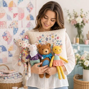 May include: A square quilted throw pillow with a floral peacock tail design, held alongside four plush toys: a floral cat, a white mouse with a purple shirt, a brown bear with a blue polka-dot bow tie, and a yellow cat with a pink bow tie.