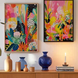 May include: Two framed abstract paintings with bright colours and bold brushstrokes, a blue ceramic vase, three smaller vases, and two books on a wooden shelf.