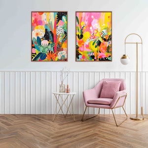 May include: Two abstract paintings with bright colours and floral patterns hang on a white wall above a pink armchair and a gold side table. The paintings are framed in gold.