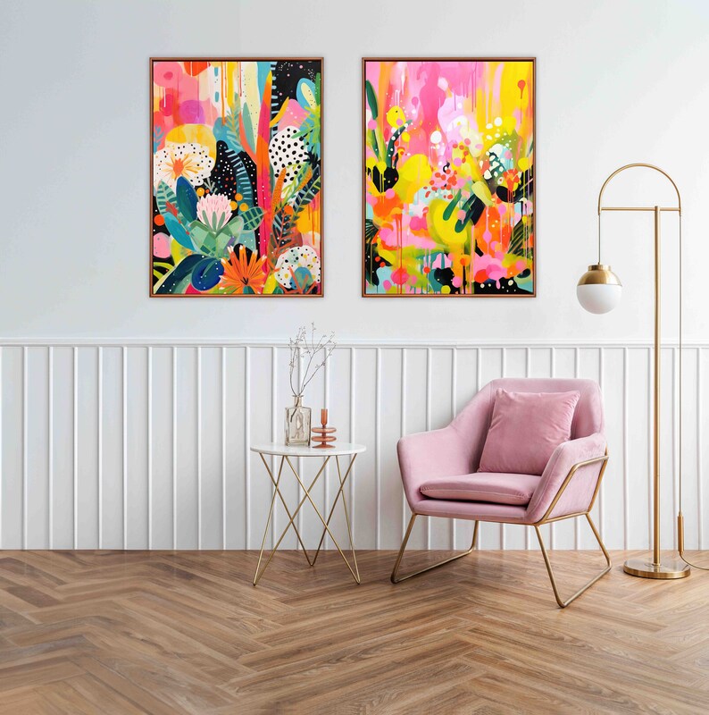 May include: Two abstract paintings with bright colours and floral patterns hang on a white wall above a pink armchair and a gold side table. The paintings are framed in gold.