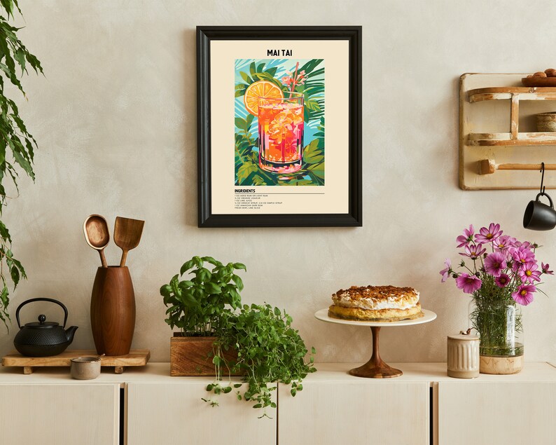May include: A framed poster with a colorful illustration of a Mai Tai cocktail. The poster has the title "Mai Tai" and a list of ingredients. The poster is hanging on a white wall above a wooden shelf with a cake stand and a vase of flowers.