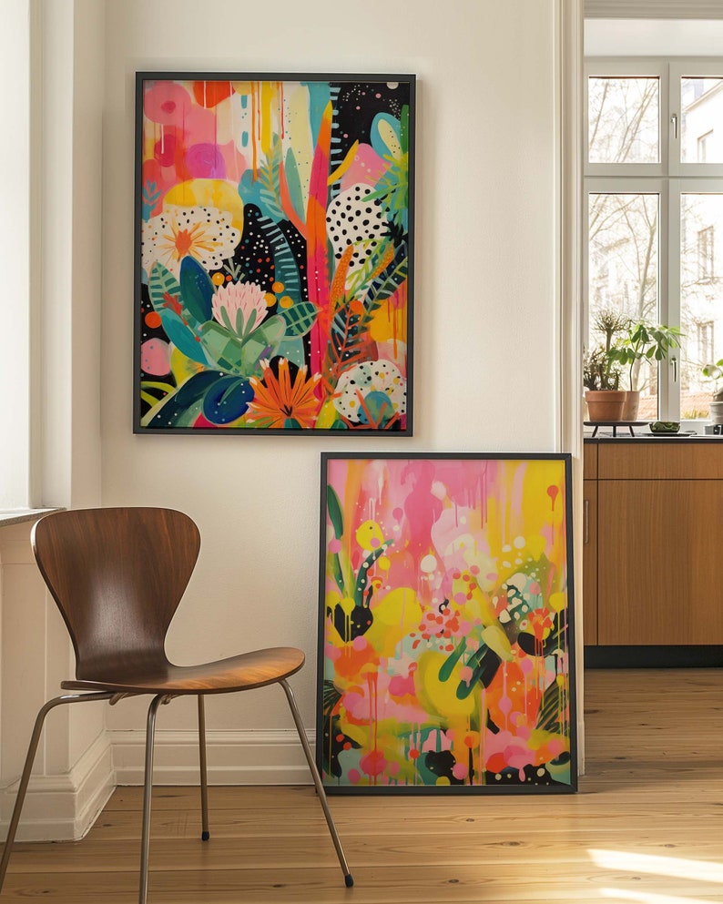May include: Two framed abstract paintings with bright colours and bold patterns. The paintings feature a mix of pink, yellow, green, and black. The paintings are hung on a white wall.