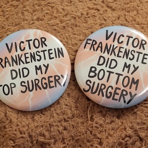 Peut inclure: Deux badges ronds avec un motif rose pastel, bleu et blanc. Les badges portent les textes "VICTOR FRANKENSTEIN DID MY TOP SURGERY" et "VICTOR FRANKENSTEIN DID MY BOTTOM SURGERY" en noir.