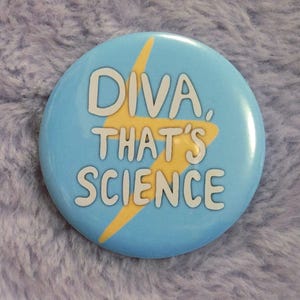 May include: A round, light blue button with the text "DIVA, THAT'S SCIENCE" in white lettering. A yellow lightning bolt graphic is behind the text. The button is a fun accessory.