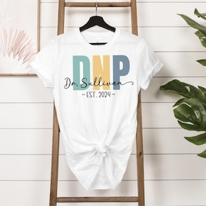May include: White t-shirt with a colorful DNP design and the text "Dr. Sullivan ~EST. 2024~" printed on the front.