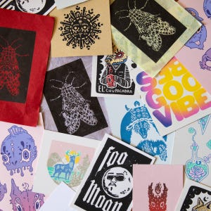 May include: A collection of colorful art prints featuring various designs. The prints include images of moths, suns, a deer in a landscape, and the text "Good Vibes". The color palette includes red, black, blue, pink, and yellow.