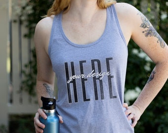 May include: A heather grey tank top with a black and white graphic that says "HERE your design". The model is holding a blue water bottle.
