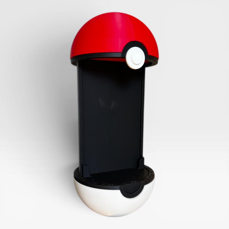 Puede incluir: Un soporte vertical para smartphone dise&ntilde;ado con la forma de una esfera roja y blanca. La mitad superior es roja con una banda negra y un bot&oacute;n circular blanco, mientras que la mitad inferior es blanca. Un panel negro sirve de soporte.