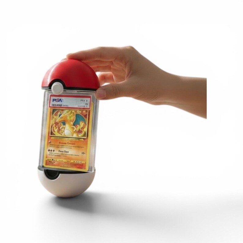 Puede incluir: Una funda protectora rectangular transparente para tarjetas coleccionables, con un dise&ntilde;o esf&eacute;rico rojo y blanco en la parte superior e inferior que recuerda a una Pok&eacute; Ball. La funda contiene una tarjeta Charizard graduada PSA con texto.